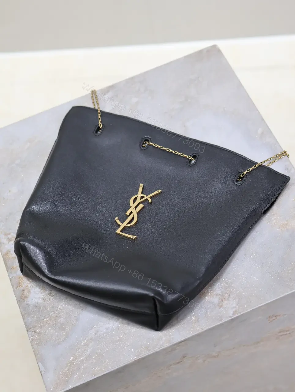 View 5 of Black leather bucket bag with gold-tone YSL monogram and chain straps for everyday luxury